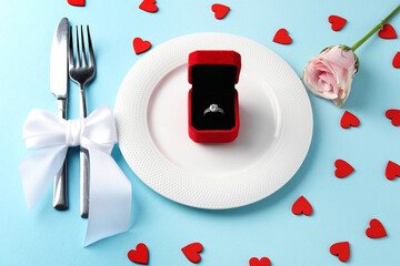 Beautiful table setting for romantic dinner, box with engagement ring and rose on light blue background