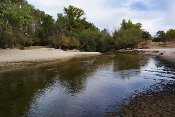 Calm river flowing through a wooded area on a clear day, reflecting nature's beauty in early afternoon light