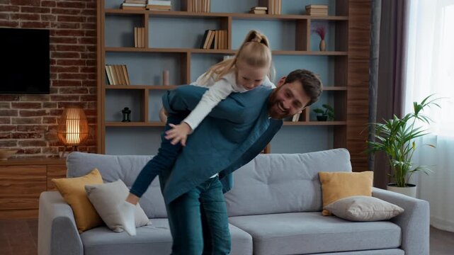 Happy Caucasian family playing at home father holding daughter piggyback dad carrying on back little girl kid child pretending airplane flying funny play having fun fooling together childcare game