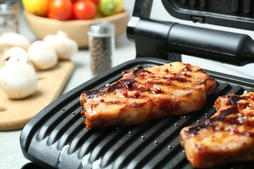 Electric grill with delicious steaks on light table in kitchen, closeup