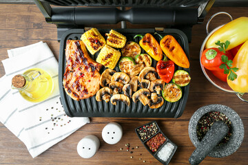 Electric grill with steak and vegetables on wooden table in kitchen, flat lay