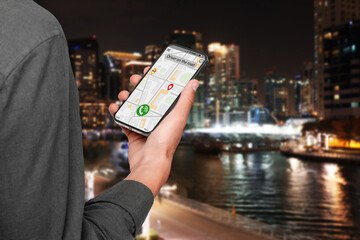 Man using app on mobile phone to call taxi on city street in evening, closeup