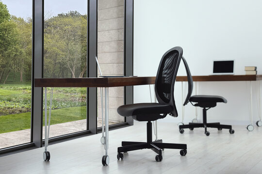 Black chair, laptop and desk in office near window - Powered by Adobe