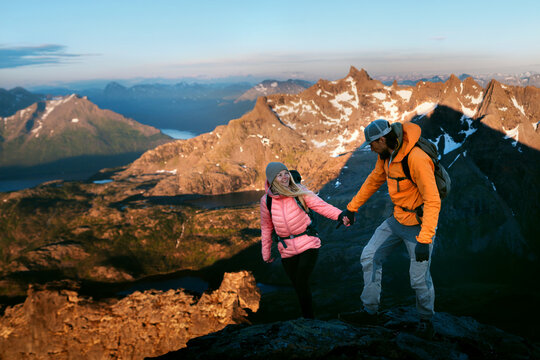 Couple hiking hand in hand through Norway mountains - travel healthy lifestyle friends on extreme vacations romantic hiking tour, active people enjoying sunset aerial views adventure journey in wild - Powered by Adobe