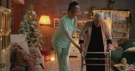 Kind caregiver supporting elderly woman walking with walker in festive living room during Christmas, showing care and gentle assistance. - Powered by Adobe