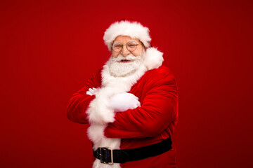 Happy Santa in a red suit with white fur trim smiles with arms crossed against a bold red background perfect for Christmas holiday promotion