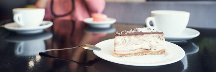 Delicious slice of marbled cheesecake with chocolate glaze and coffee in a cozy cafe setting.