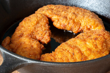 Southern fried chicken cooked in a cast iron frying pan with cooking oil. On a wooden board background..