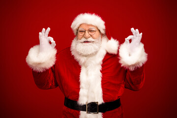 Santa Claus in a classic red suit with white fur trim smiles and makes an ok sign against a deep red background for a festive holiday scene