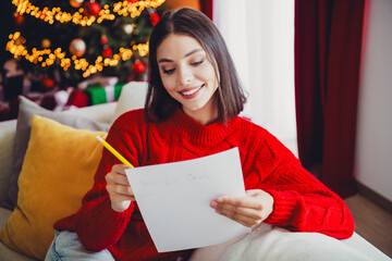 Whimsical holiday moment as a woman smiles while writing New Year goals beside a twinkling christmas tree in a cozy home scene