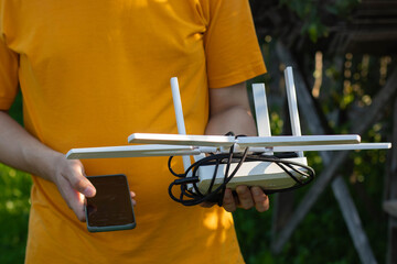 A man in an orange T-shirt holds a mobile phone in one hand and a router in the other to connect to the internet.