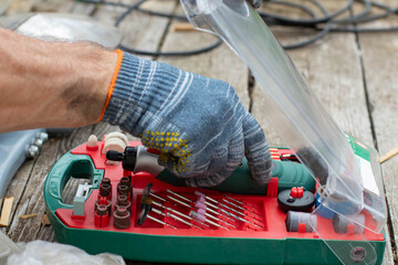 A man pulls a Dremel out of a box. The Dremel and its attachments are in a plastic box.