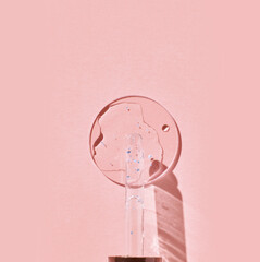 Glass dropper with serum casting shadow on soft pink background minimalist skincare concept.