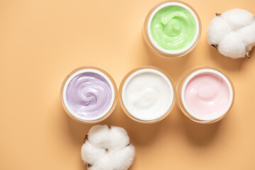 Set of colorful cosmetic creams in jars on yellow pastel background, top view