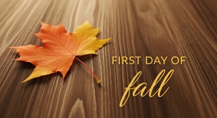 A single, vibrant maple leaf rests on a wooden surface, announcing the first day of fall