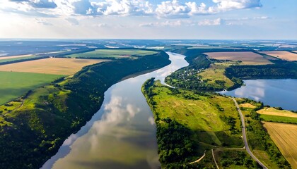 Aerial view of a winding river flowing through diverse farmlands and lush green fields under a sunny sky with fluffy clouds