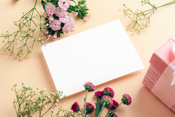 Blank card and gift box with flowers on beige background. Top view, mockup