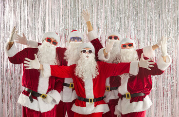 Santa team in festive costume shares cheer. Six Santas in sunglasses spread arms as a group before...