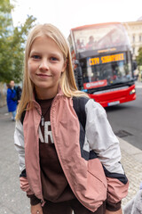 Portrait happy smiling teenager girl stands Europe city street red double decker bus background. Casual pink jacket blond hair urban backdrop highlight youthful travel mood  friendly school trip vibe