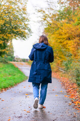 Obraz premium Woman in blue coat walks down a path in autumn, fall foliage