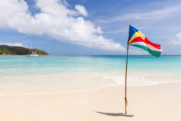 A sunny tropical beach scene featuring Seychelles flag planted in white sand