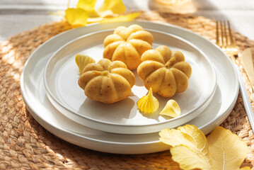 Pumpkin-Shaped Mini Cakes with Cream and Autumn Decor on Woven Placemat