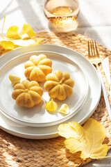Pumpkin-Shaped Mini Cakes with Cream and Autumn Decor on Woven Placemat
