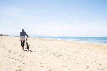 Frau schiebt Fahrrad am Strand  © christophe papke