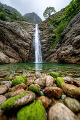 Beautiful waterfall cascading into a clear, green pool surrounded by rocky slopes and lush greenery in a serene mountain landscape