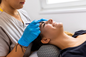 Obraz premium Young female client receiving a professional brow lamination (also known as a non-surgical brow lift) in a clean, modern beauty salon.