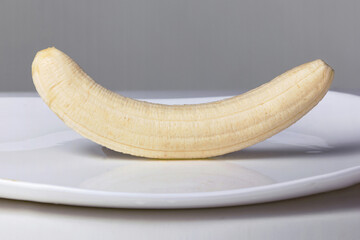 A close-up of a banana lying on a glossy white plate, which will soon be doused with chocolate. T-series of 9 photos, the first photo.
