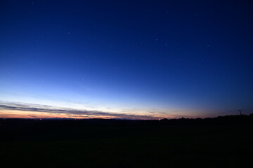 Beautiful colorful sunset over the Czech landscape with blue and red sky tones blending into the first visible stars. A scenic view of mountain silhouettes and twilight sky, capturing the peaceful tra