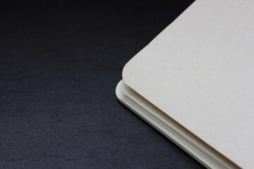 White closed notebook corner lying on dark background, horizontal photo. Stationery, empty pages for notes, blank paper sheets, office and business concept