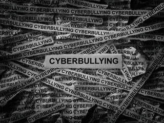 Strips of newspaper with the words Cyberbullying typed on them. Black and white. Close up.