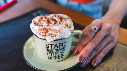 Happy young woman holding a rustic ceramic mug with a gourmet coffee drink topped with whipped...