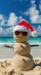 A sand snowman wearing a red Santa hat and sunglasses stands on a tropical beach. The ocean and blue sky create a festive holiday atmosphere.