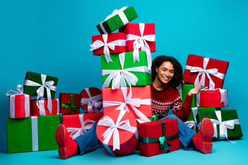 Playful multiethnic girl enjoys festive christmas gift pile and colorful presents in a bright blue...