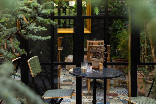 patio table and chairs tucked away in a cozy, leafy indoor outdoor cafe with mirror doors and lots of green and tile floors in europe