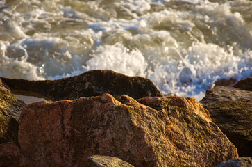 Sunlit Coastal Rocks in Foreground with Dynamic Foaming Waves Crashing in Background