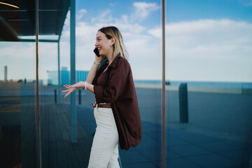 Obraz premium Smiling woman on smartphone call, using hand gesture while walking, symbolizing friendly communication, mobile lifestyle, joyful digital connection and positive conversation.