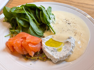 Close-up view of salmon fillet with spinach leaves and creamy dill sauce on a white plate. Gourmet dining, healthy meal, and refined culinary aesthetics.
