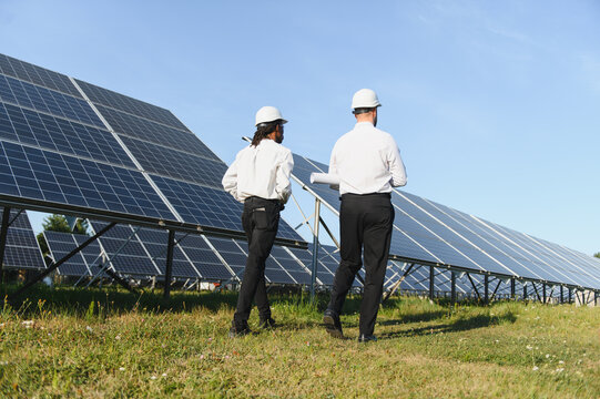 Engineers inspecting solar panels at renewable energy farm - Powered by Adobe