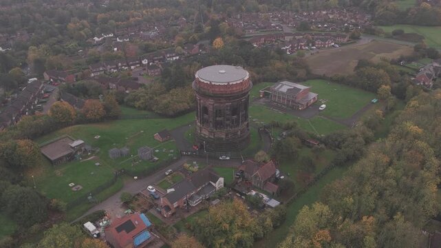 Overhead aerial footage panning right to left of Norton water tower. a brick built old water storage system around the Liverpool region. Grade II victorian architecture with houses, trees, fields.