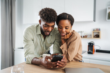 African american couple using mobile phone in kitchen