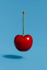 Fresh red cherry floating against a vibrant blue background