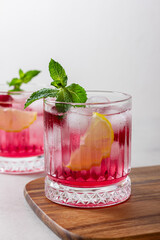 Raspberry gin and tonic with ice in a glass on a light background