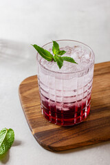 Cocktail with ice in a glass on a wooden cutting board