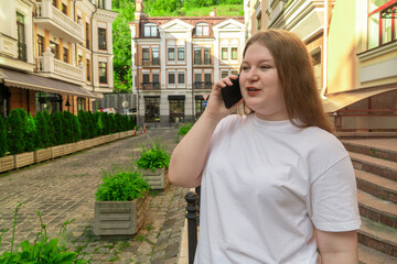 Confident plus-size woman using her mobile phone for a conversation while standing on a cobblestone street surrounded by classic European buildings