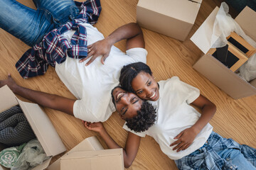 Happy couple lying on the floor surrounded by moving boxes, relaxing after unpacking in their new home and daydreaming about their future together