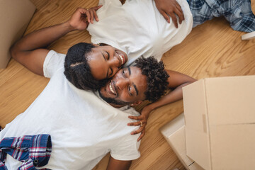 Happy couple lying on the floor surrounded by moving boxes, relaxing after unpacking in their new home and daydreaming about their future together